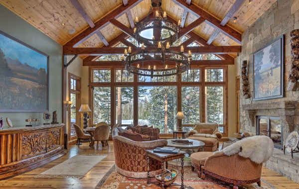Interior shot of a luxury vacation rental in the U.S. with large windows, overstuffed furniture, and a beautiful view of trees and snow