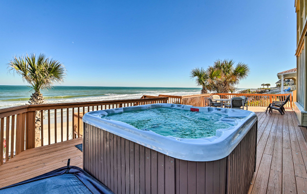 A hot tub on a large wraparound porch with a gorgeous view of the beach, ocean, and palm trees