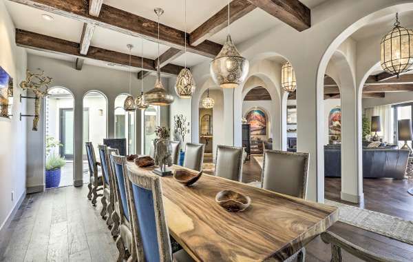Interior shot of a luxury vacation rental dining room with a long dining table, 12 chairs, and overhead pendants providing soft lighting 