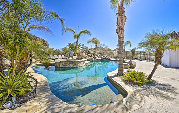 Exterior shot of a beautiful pool with a hot tub, surrounded by palm trees and a bright sunny sky