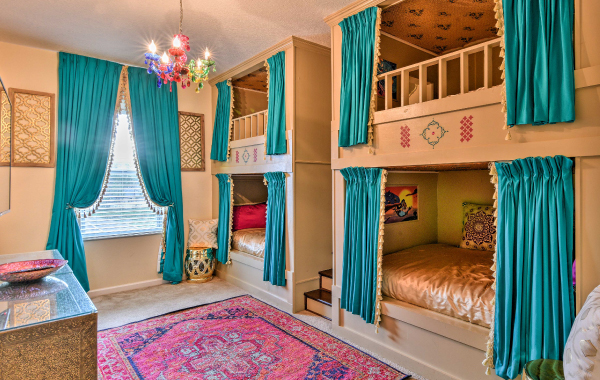 Interior shot of a Disney-themed kids room with several bunk beds, a colorful rug and pendant light, and teal curtains